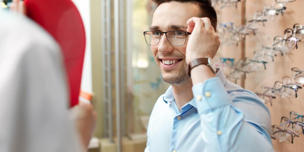 man trying on prescription glasses in an optician's shop
