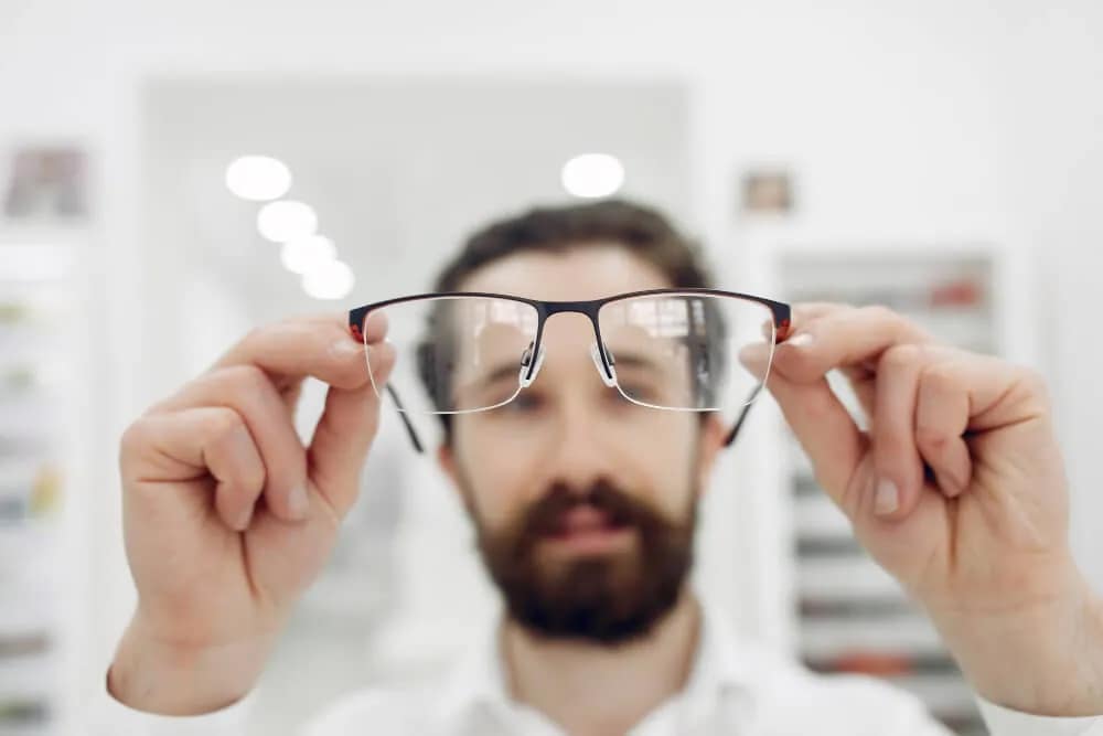 man holding up Prescription Glasses to the light