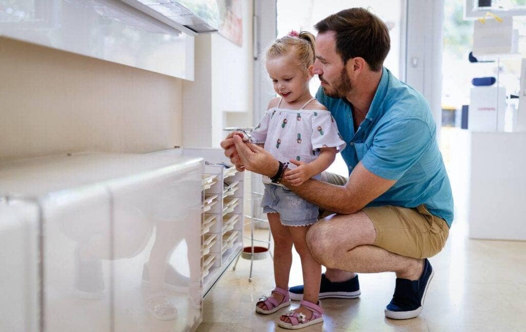 Health care, eyesight and vision concept. Little girl choosing glasses with father at optics store