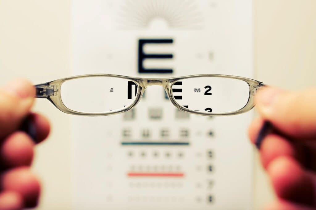 Prescription Glasses being held up in front of eye testing chart