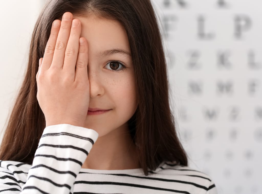 Young girl with hand over one eye, optician chart in background