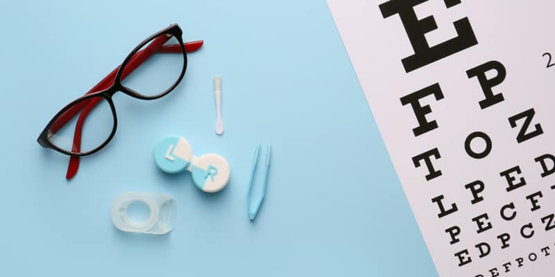 optician eye test chart on light blue table next to prescription glasses and contact lens kit